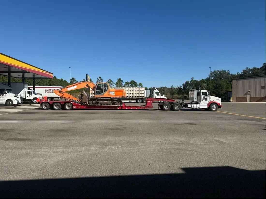 Orange excavator on a lowboy trailer behind a Kenworth tractor